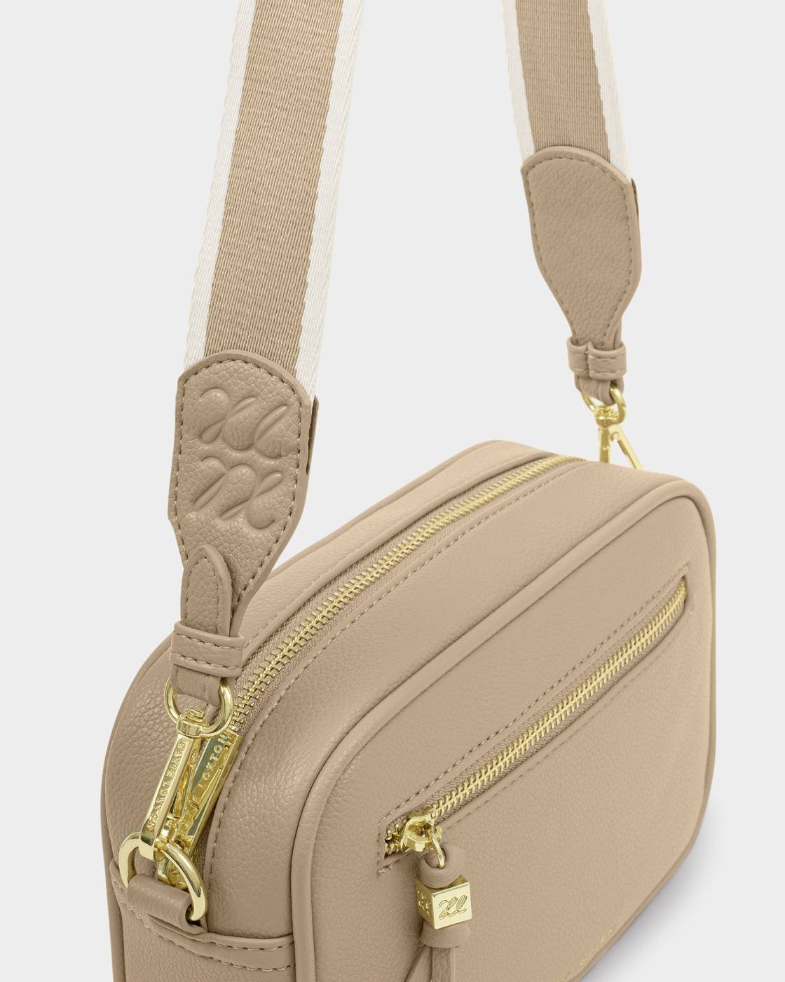 Beige crossbody bag with gold zippers on a light gray background