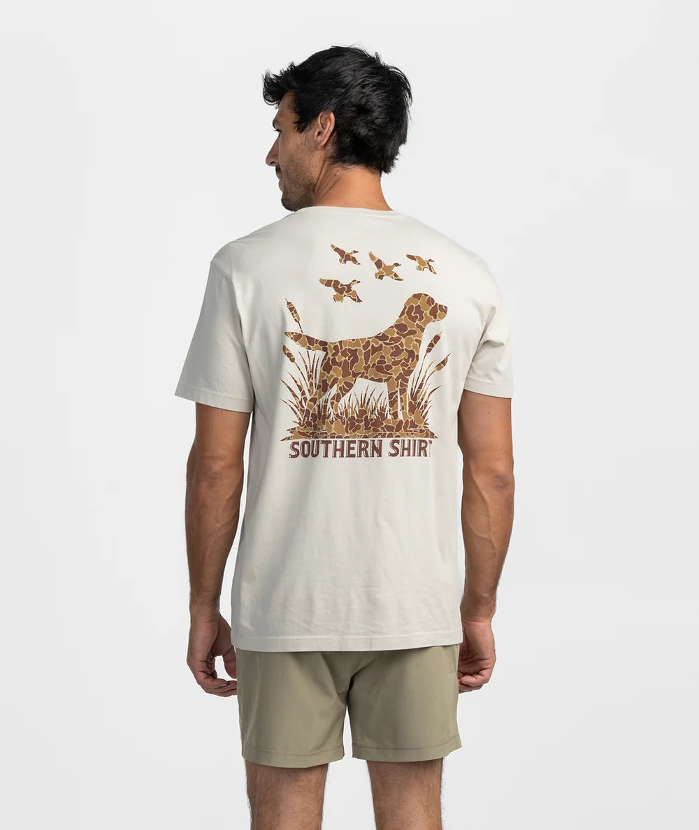 A man viewed from the back wearing a cream-colored t-shirt with a large graphic on the back featuring a dog, ducks, and the text 'SOUTHERN SHIR'.
