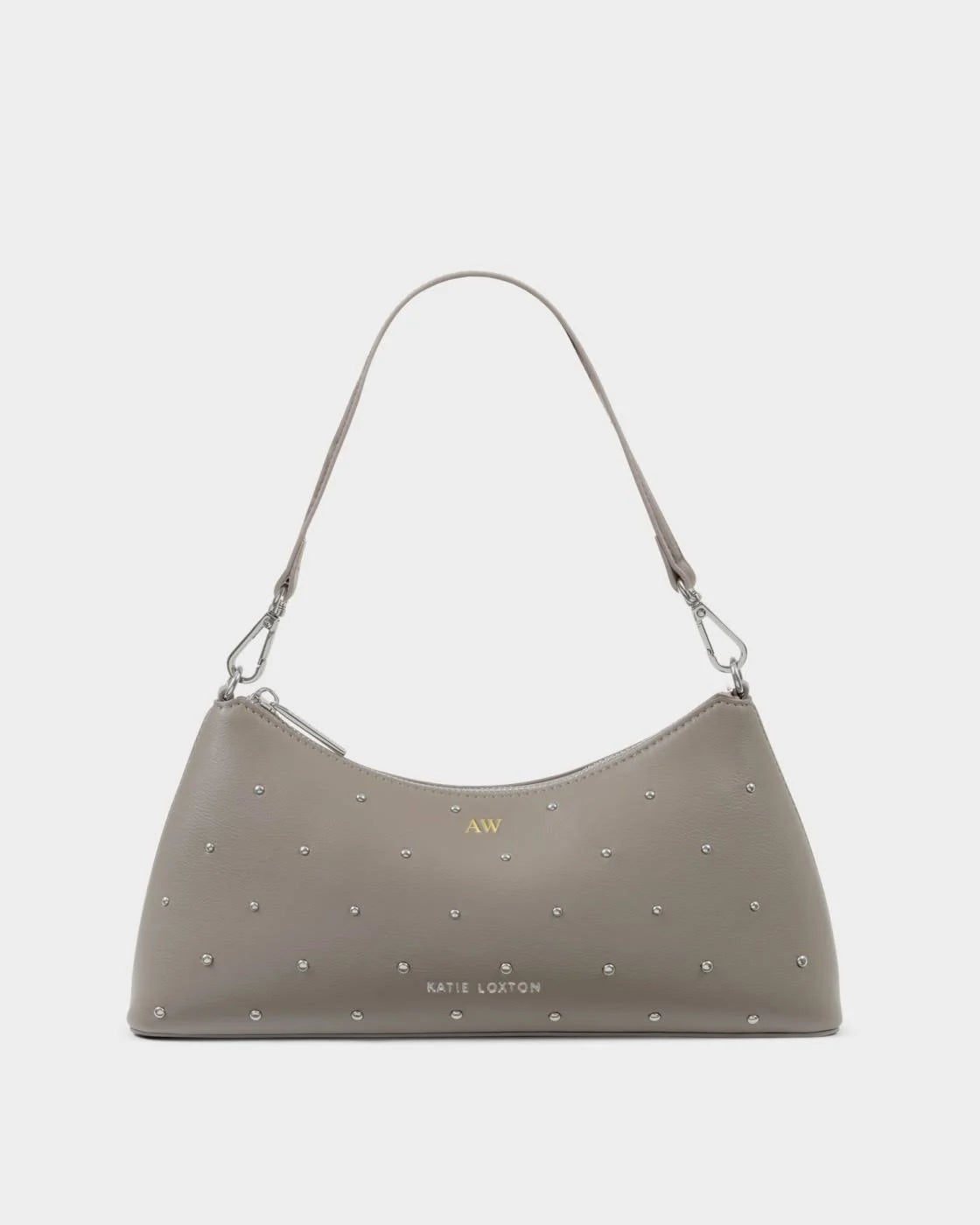 A taupe-brown studded shoulder bag by Katie Linton, featuring a crescent-shaped silhouette, a single shoulder strap, and silver-tone studs across the surface, set against a plain light gray background.