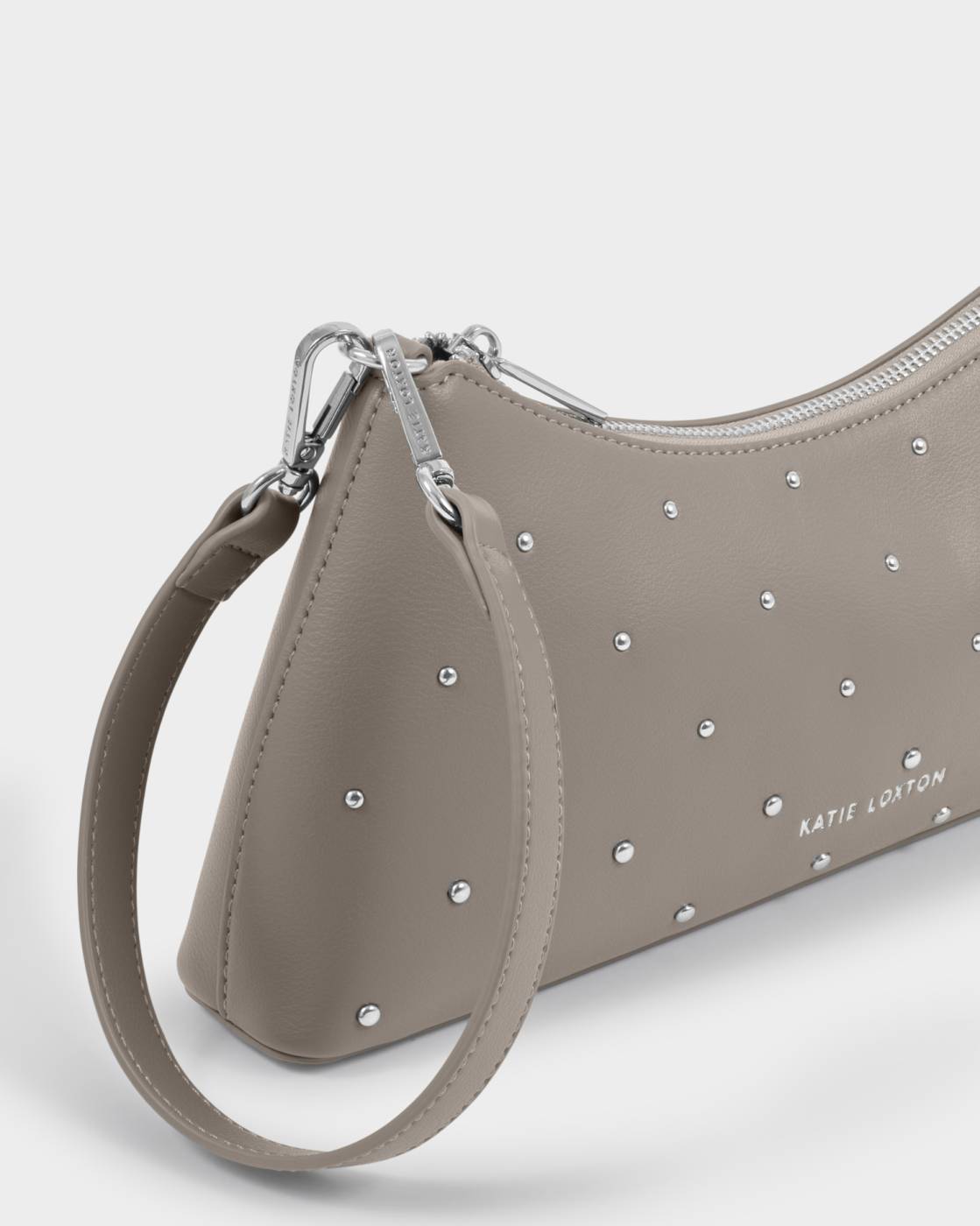 A close-up of a taupe leather wristlet clutch by Katie Loryson, decorated with silver studs and featuring a matching leather wrist strap with silver hardware.
