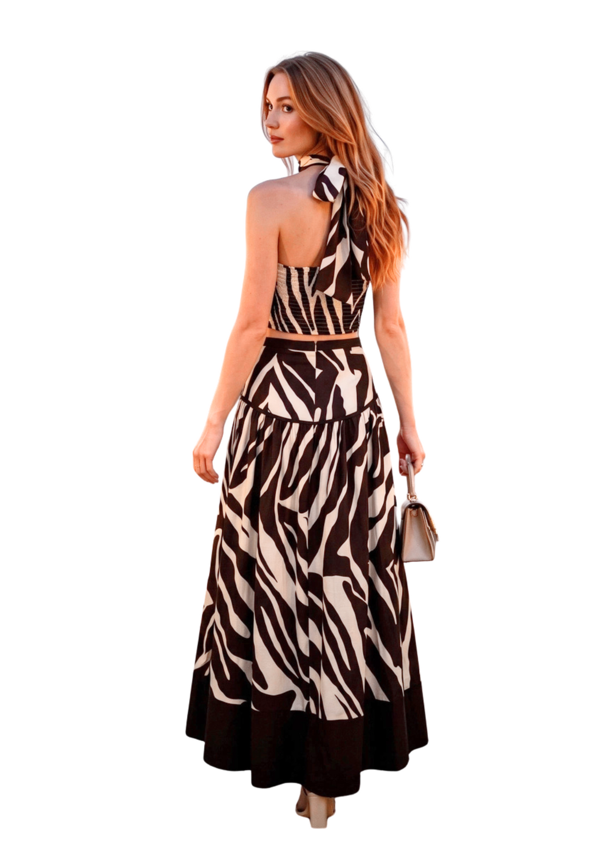 Woman wearing a brown and white zebra print halter top with a matching maxi high waisted skirt in front of a white background. 