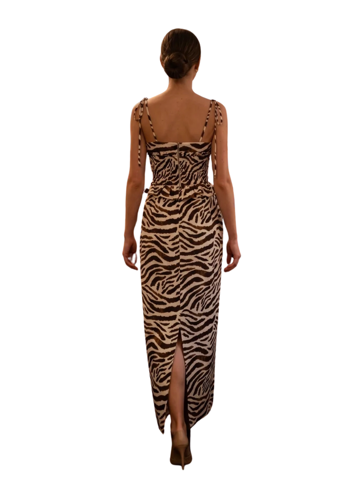 A woman viewed from behind wearing a sleeveless zebra-print maxi dress with a high slit and tie straps at the shoulders, set against a plain white background.