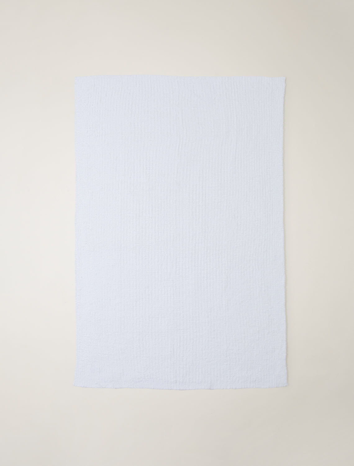 A light textured blanket laid flat against a neutral cream-colored background.