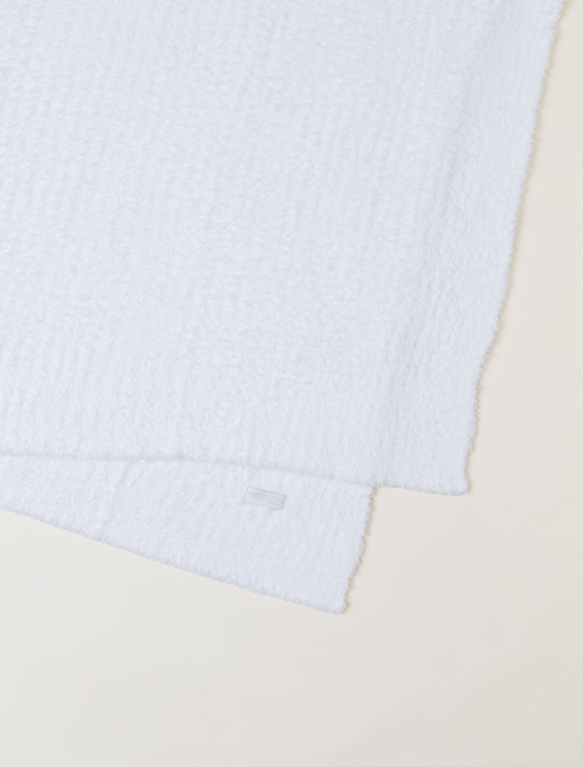 A close-up of a white textured blanket, folded diagonally on a light beige background.
