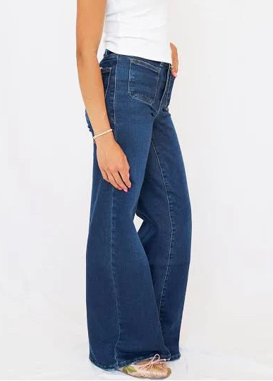 A woman modeling a pair of dark blue wide-leg jeans with a white sleeveless top, standing against a plain white studio background.
