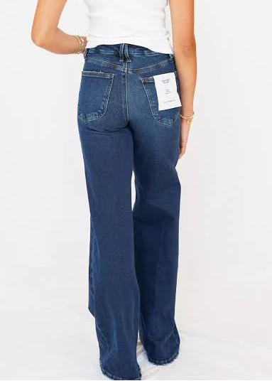 A woman shown from the back wearing dark blue wide-leg jeans and a white sleeveless top, standing against a plain white studio background.