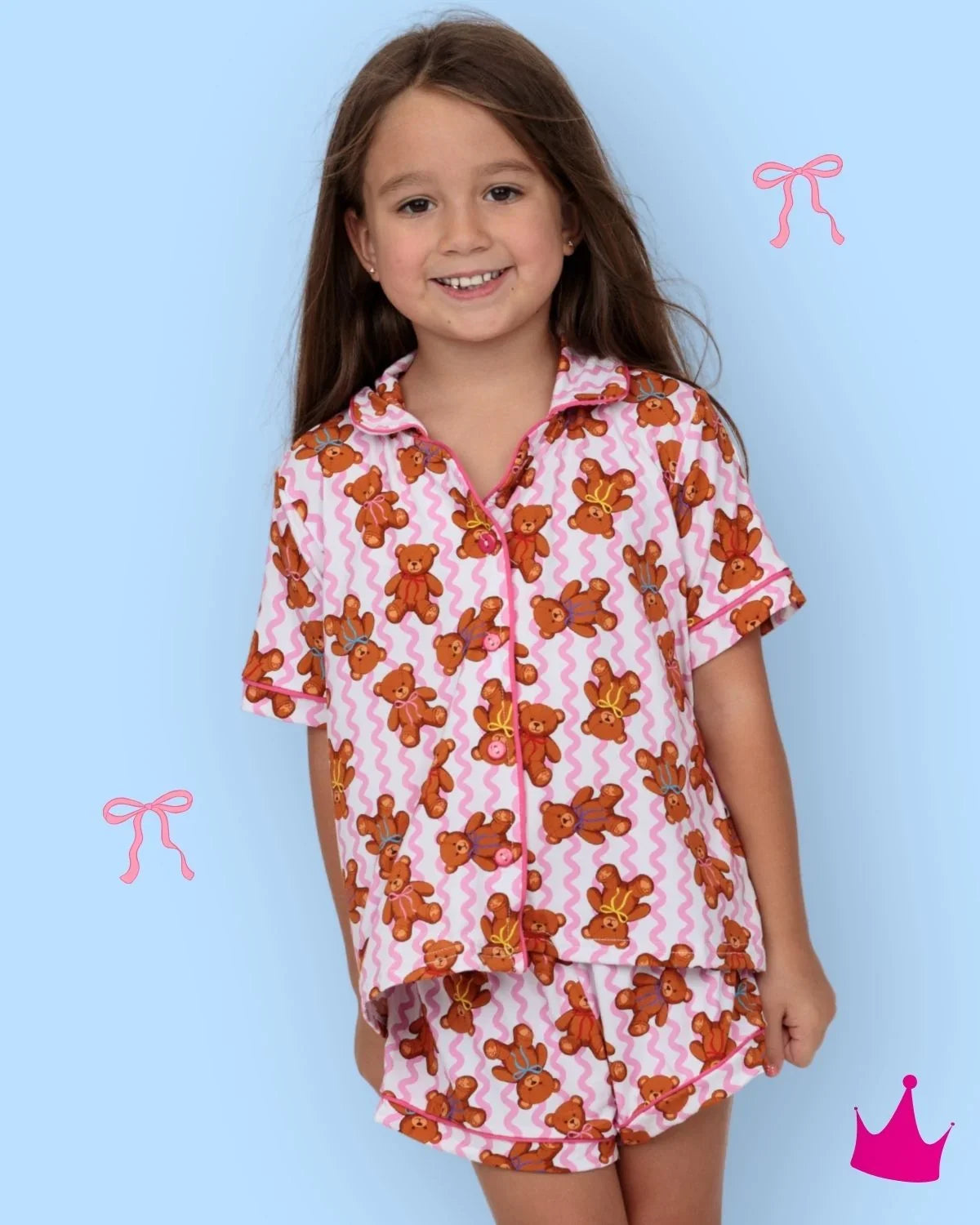 A young girl smiling while wearing a two-piece pajama set. The pajama set features a pink and white chevron pattern with orange teddy bears printed all over it.