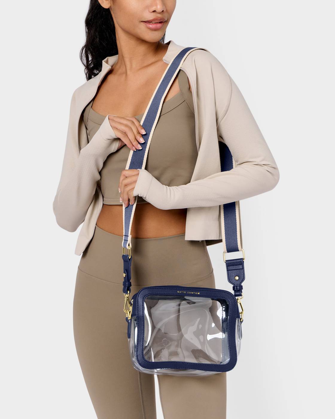 Woman holding a clear handbag with blue straps against a white background