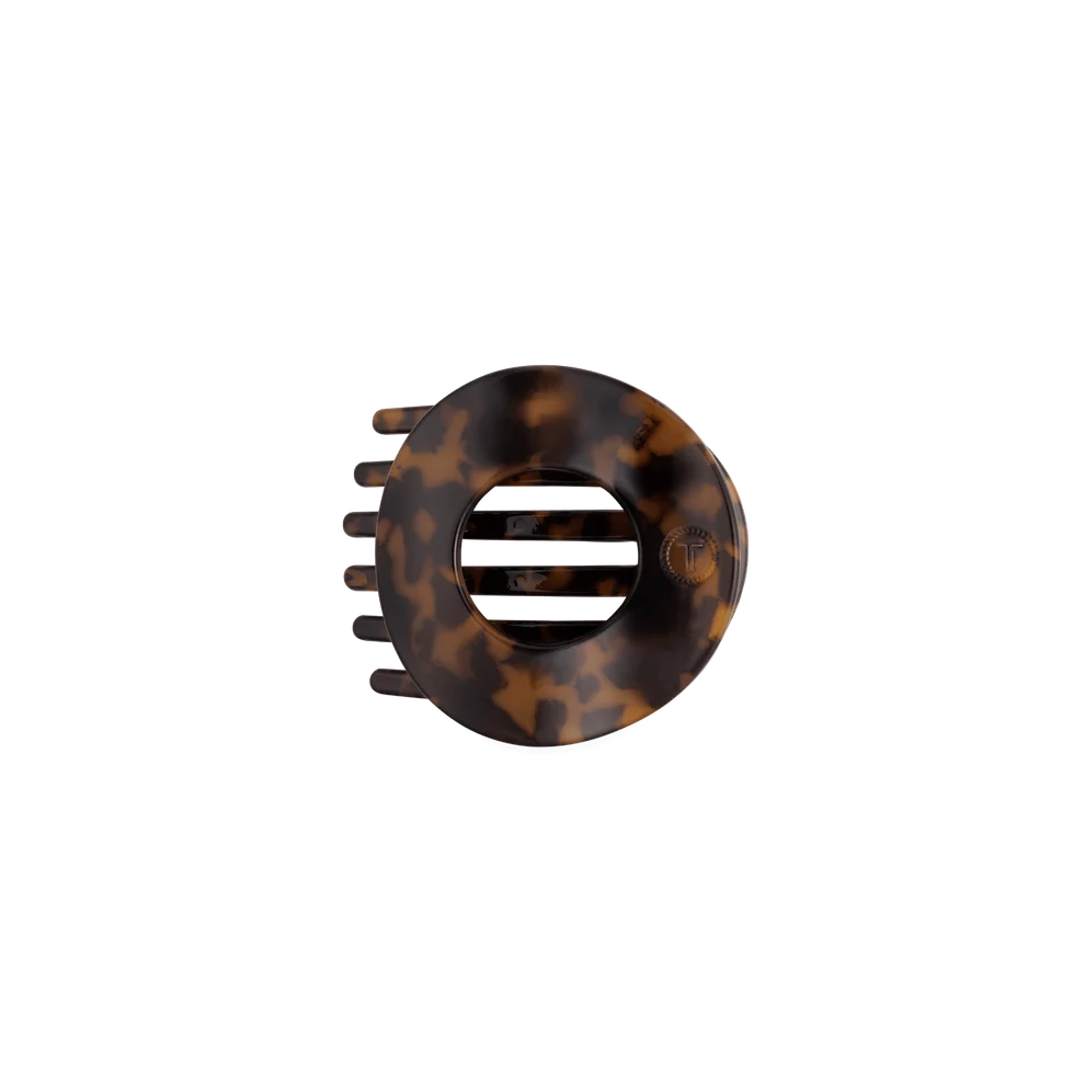 A circular hair claw clip in a classic tortoiseshell pattern, featuring a central ventilation slot and five outer teeth, shown against a plain white background.