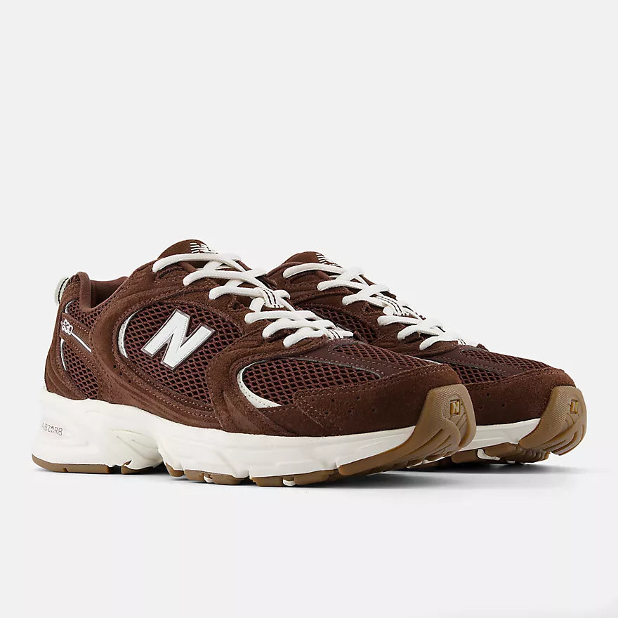 A pair of New Balance 574 sneakers in brown suede and mesh with white laces, white midsoles, and brown rubber outsoles, photographed on a light gray studio background.