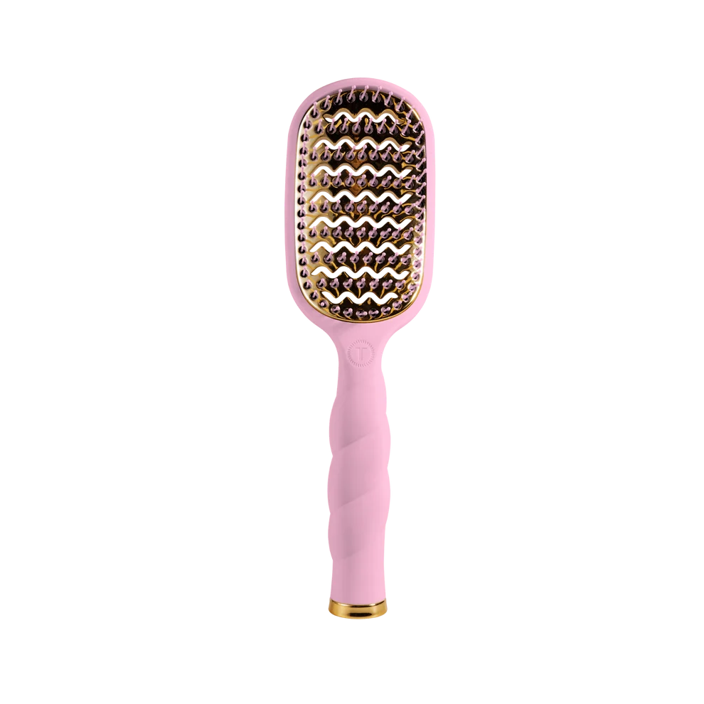 A pink hairbrush with a twisted handle, gold metal bristles, and a gold base, shown against a plain white background.