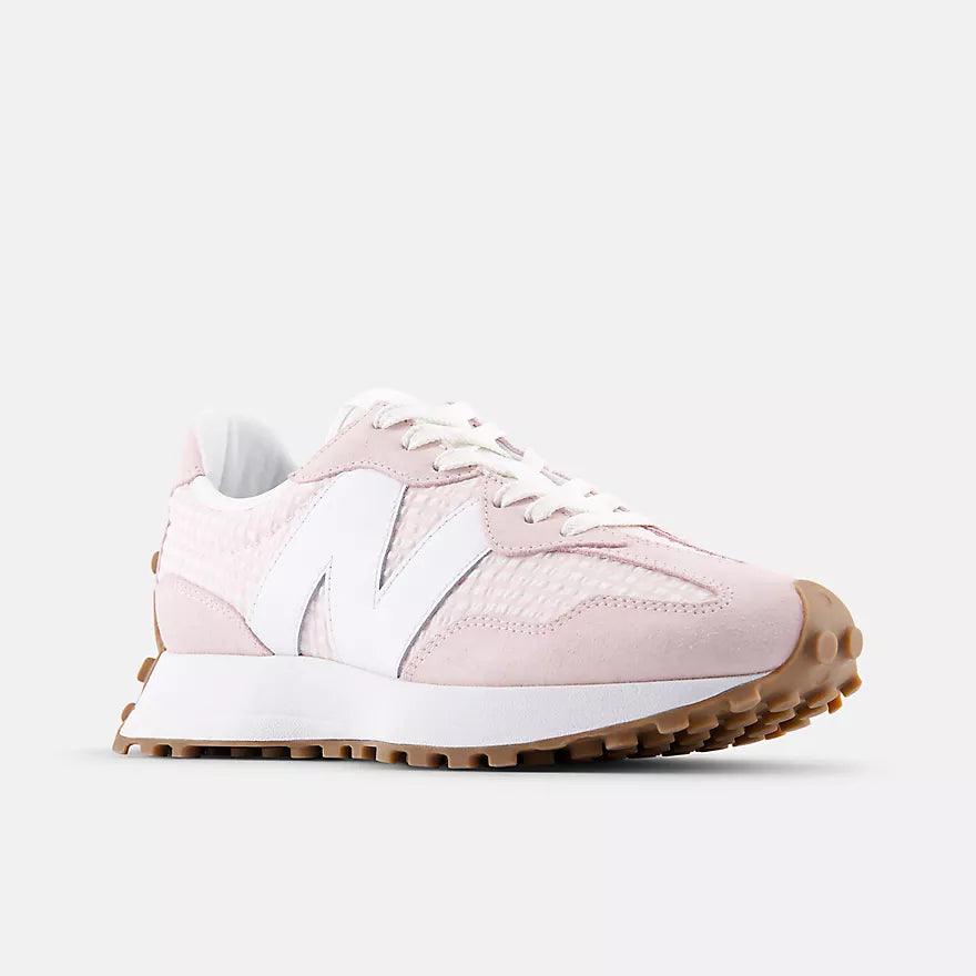 A light pink New Balance sneaker with white laces, a white side logo, and a brown gum sole, shown from a side profile on a light gray background.